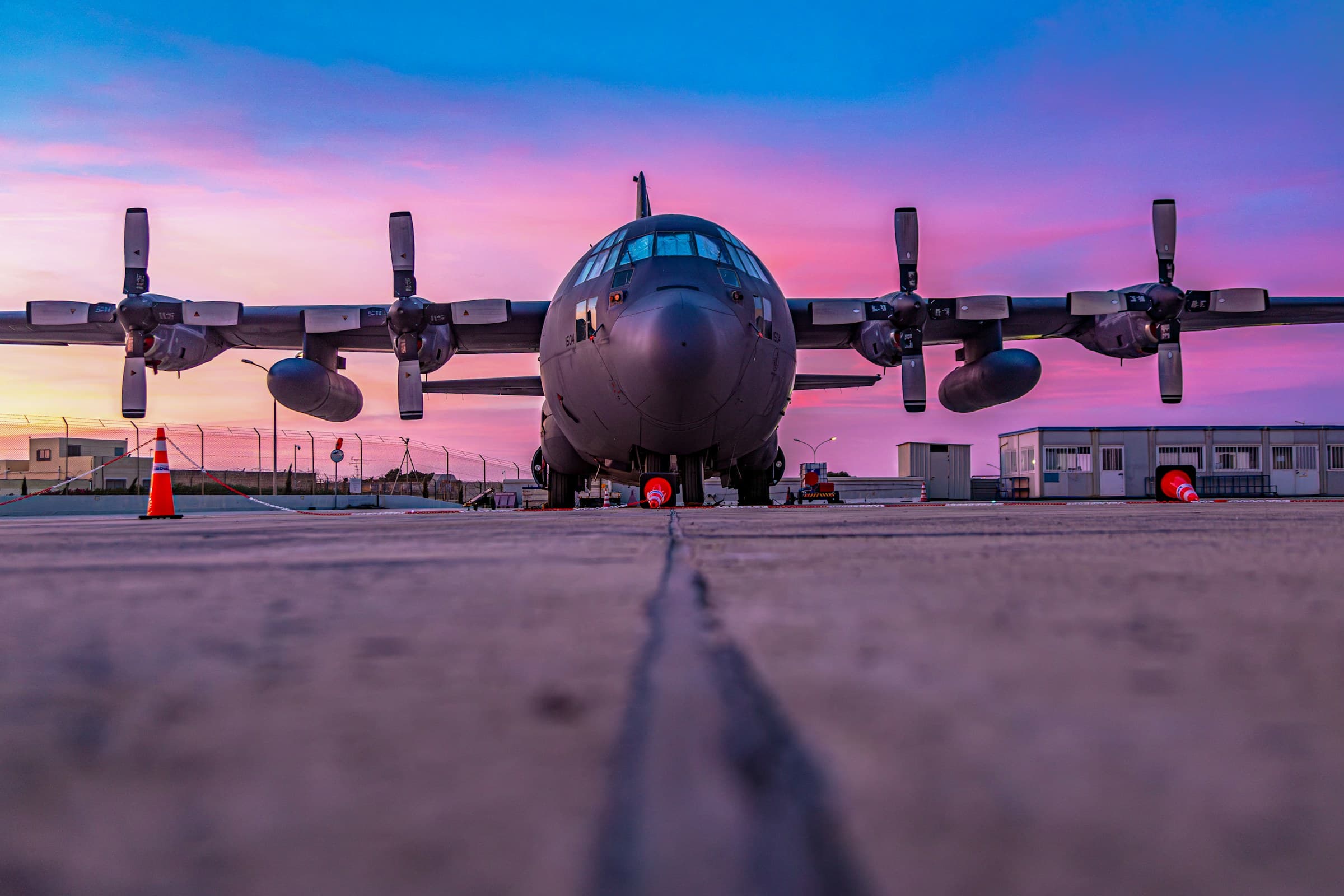Military C-130 cargo transport aircraft parked on the flight line at sunset