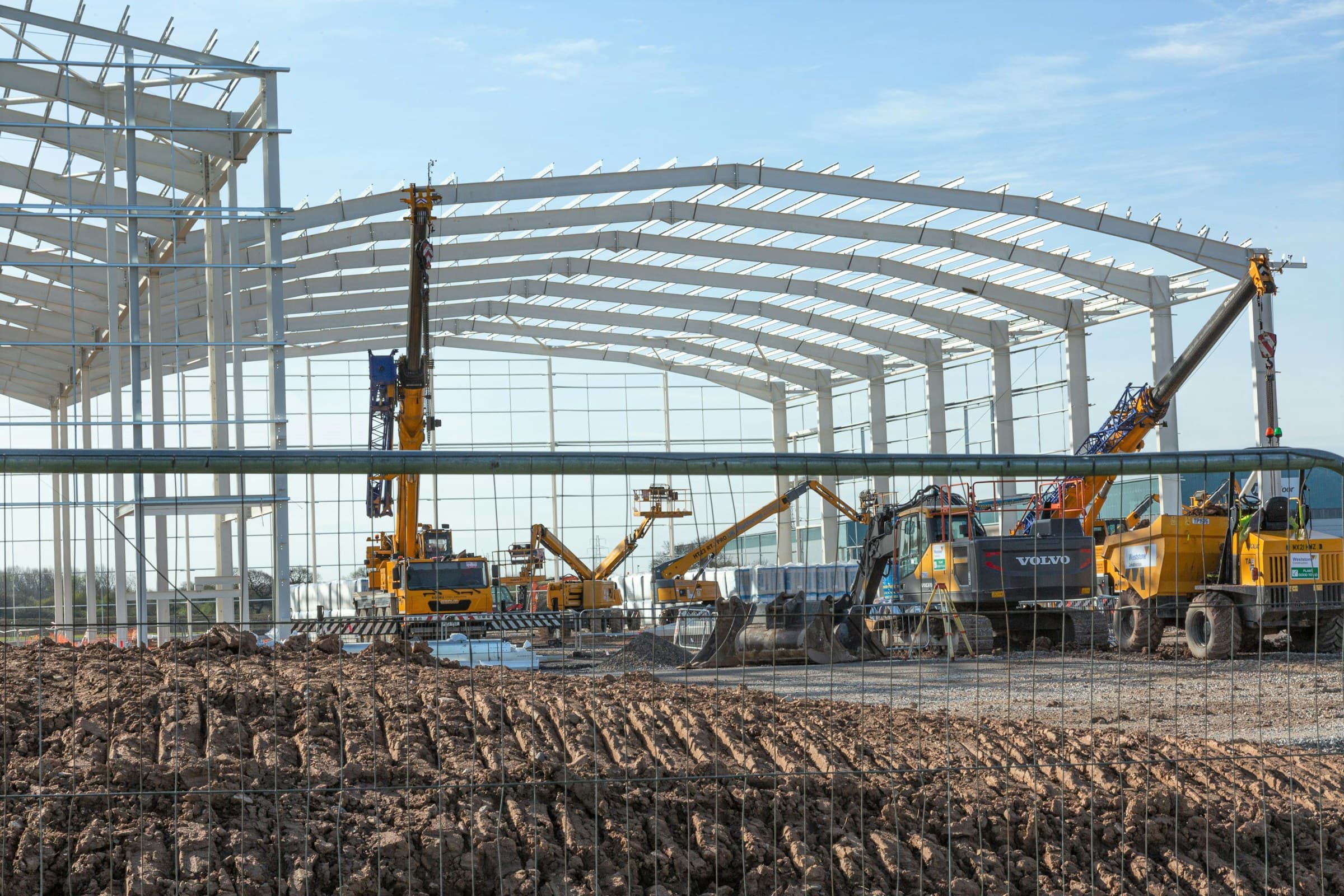 Excavators and cranes working at a steel-frame commercial building construction site under a clear sky