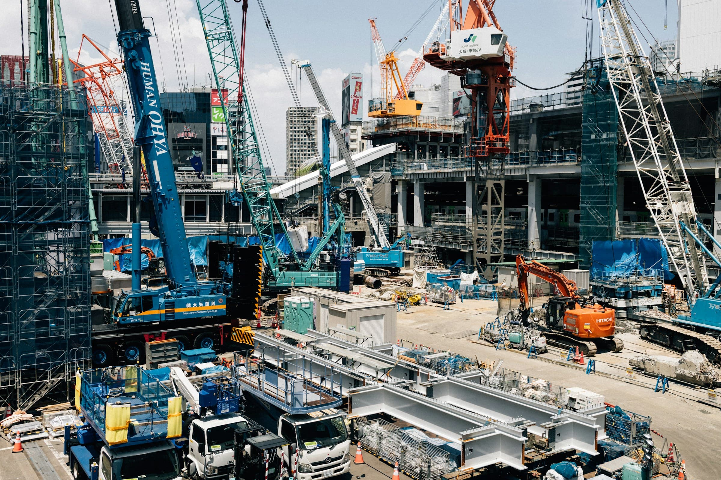 Aerial view of a large construction project with tower cranes, trucks, and active earthwork